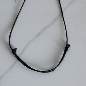 May include: A simple black cord necklace with a slip knot closure.