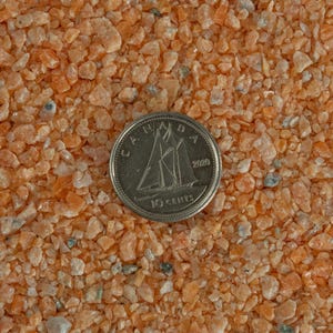 May include: Close-up of orange and white crushed stone, with a Canadian 10-cent coin for scale. The coin is dated 2000.