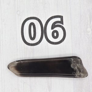 May include: A dark, rectangular object with a rounded end and a small hole, possibly a handle or attachment point. The number "06" is printed above the object in a bold, black font.