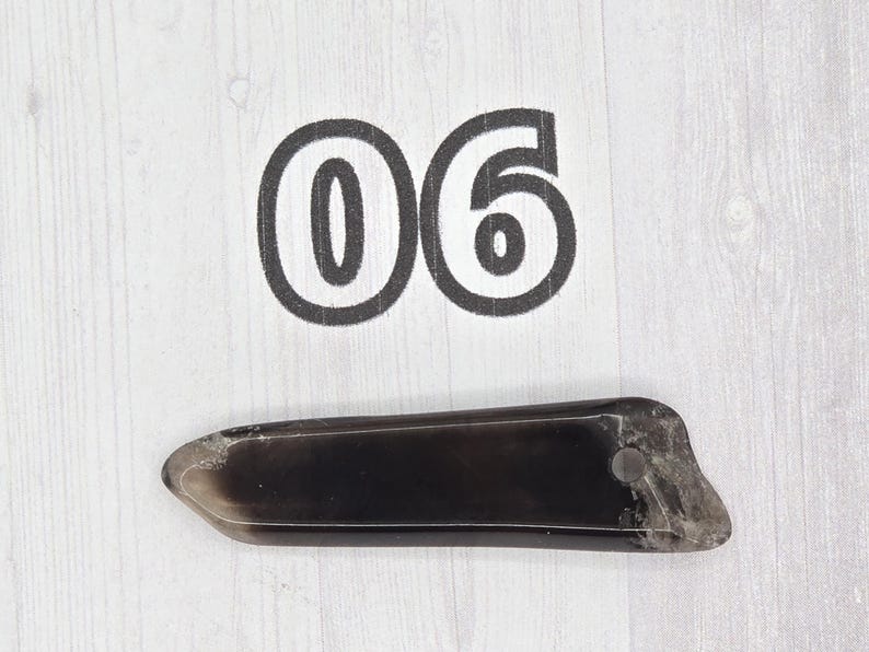May include: A dark, rectangular object with a rounded end and a small hole, possibly a handle or attachment point. The number "06" is printed above the object in a bold, black font.