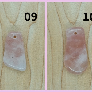 May include: Two pink rose quartz pendants with a hole at the top for stringing. The pendants are on a light brown wooden surface. The numbers 09 and 10 are written above the pendants.