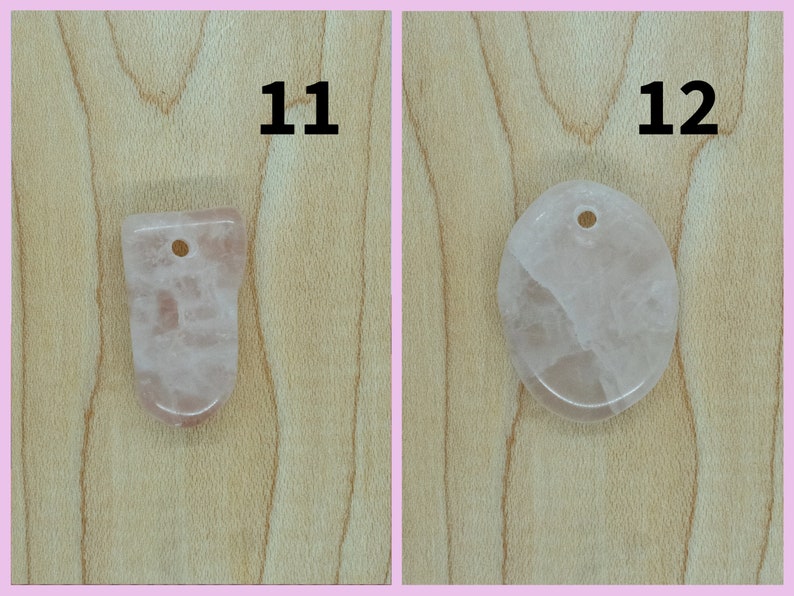 May include: Two pink rose quartz pendants with holes for hanging. The pendant on the left is a freeform shape, and the pendant on the right is oval shaped. Both pendants are on a light brown wooden surface.