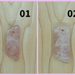 May include: Two pink rose quartz pendants with a hole drilled at the top for stringing. The pendants are on a light wood background. The pendants are labeled 01 and 02.