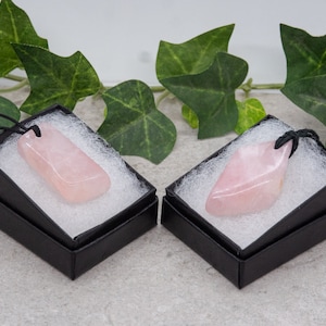 May include: Two pink rose quartz pendants with black cords, displayed in black gift boxes with white inserts.