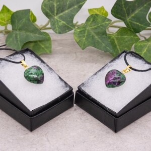 May include: Two heart-shaped green and pink gemstone pendants on black velvet cords in black gift boxes.