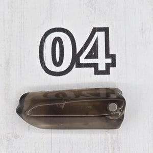 May include: A dark, translucent, oblong-shaped object with a small, silver-colored circular element. The number "04" is printed in black, bold font above the object. The background is a white, wood-grain pattern.