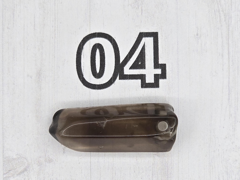 May include: A dark, translucent, oblong-shaped object with a small, silver-colored circular element. The number "04" is printed in black, bold font above the object. The background is a white, wood-grain pattern.