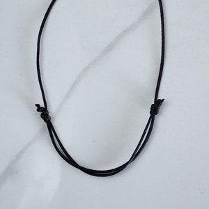 May include: A black cord necklace with a simple knot closure.