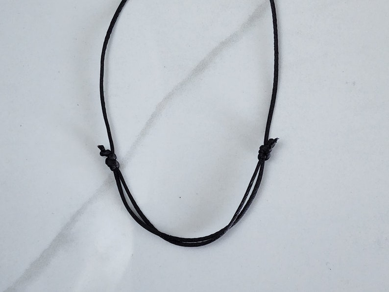 May include: A black cord necklace with a simple knot closure.