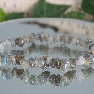 May include: A gray labradorite chip bracelet with a reflective surface. The bracelet is made of small, irregular shaped stones.