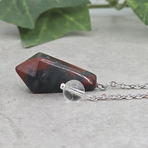 May include: A black, red and green gemstone pendulum on a silver chain. The pendulum is attached to a clear crystal ball.