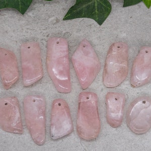 May include: A collection of 12 pink rose quartz pendants with drilled holes. The pendants are various shapes and sizes, and have a natural, polished finish.
