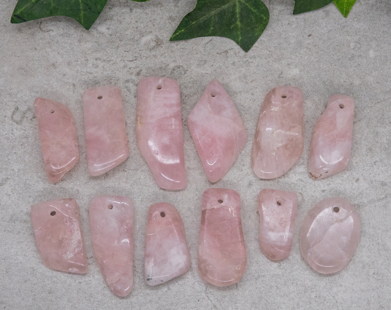 May include: A collection of 12 pink rose quartz pendants with drilled holes. The pendants are various shapes and sizes, and have a natural, polished finish.