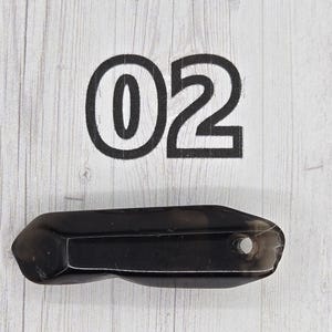May include: A dark, faceted crystal wand with a small hole at one end. The number "02" is printed in large, bold, black font above the crystal on a light wood-grain background.