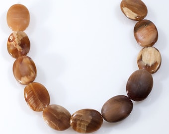 Puede incluir: Una hebra de cuentas de piedras preciosas ovaladas, de color marrón y beige. Las cuentas tienen un aspecto natural y orgánico y están enhebradas en un hilo transparente.