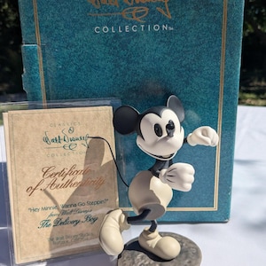 May include: A Mickey Mouse figurine from the Walt Disney Classics Collection, titled "The Delivery Boy." The figure is in a walking pose, with a black and white colour scheme. The box and certificate of authenticity are also visible.