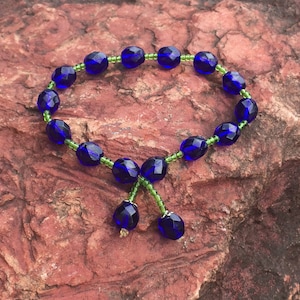 May include: A blue and green beaded bracelet with a tassel. The bracelet is made of small, round beads and has a simple design.