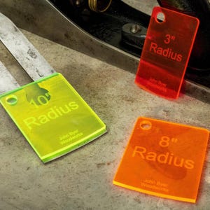 May include: Three brightly colored acrylic radius gauges: red (3-inch), orange (8-inch), and green (10-inch). Each has a hole for hanging and the text "Radius" with the maker's name. The gauges are for woodworking.