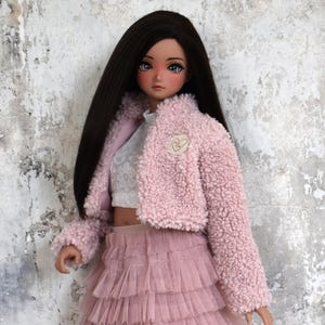 Könnte beinhalten: Eine rosa flauschige Jacke mit einem herzförmigen Patch, getragen über einem weißen Oberteil mit Blumenmuster und einem rosa Tüllrock.