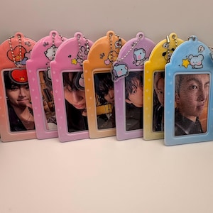 May include: A collection of six colorful photo card holders. Each holder features a different pastel color, a cartoon character, and a small photo of a person. The holders are connected by a silver chain.