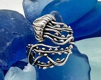 Puede incluir: Un anillo de plata con un diseño detallado de medusa. El anillo se coloca sobre un fondo de vidrio de mar azul.