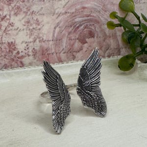 Op de afbeelding: Een paar zilveren ringen met engelenvleugels. De vleugels zijn gedetailleerd en hebben een textuur.