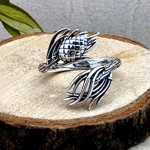 May include: A silver ring with a detailed design of a pine cone and branches. The ring is adjustable and can be worn on any finger.