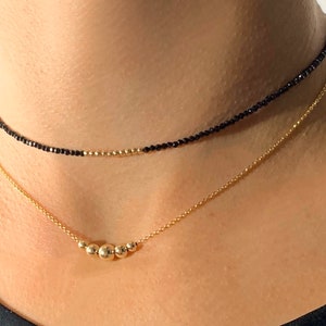 May include: Two gold necklaces, one with a delicate chain and a row of small gold beads, and the other with a black beaded choker.