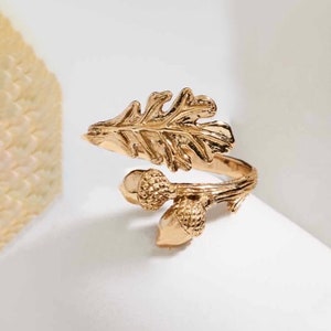 May include: A gold-toned ring with a detailed oak leaf design and two acorns. The ring is adjustable and can be worn on any finger.