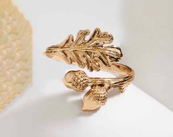 Puede incluir: Un anillo dorado con un diseño detallado de hoja de roble y dos bellotas. El anillo es ajustable y se puede llevar en cualquier dedo.