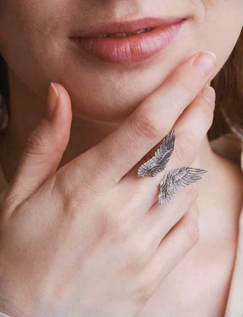 Op de afbeelding: Een zilveren ring met twee vleugels. De vleugels zijn gedetailleerd en hebben een textuur.