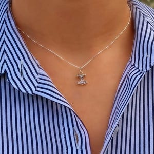 May include: A silver-coloured metal necklace featuring a small, detailed pendant shaped like a Mjolnir hammer. The pendant hangs from a thin, delicate chain that rests against the neck. The metal has a polished finish with dark oxidised accents.