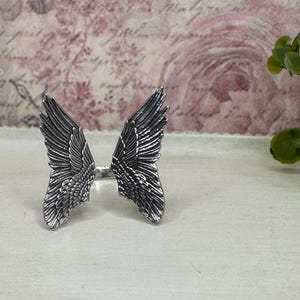 Op de afbeelding: Een zilveren ring met een gedetailleerd ontwerp van twee engelenvleugels.