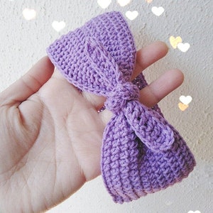 Puede incluir: Una diadema de crochet morada con un lazo. La diadema está hecha con un hilo suave y texturizado.