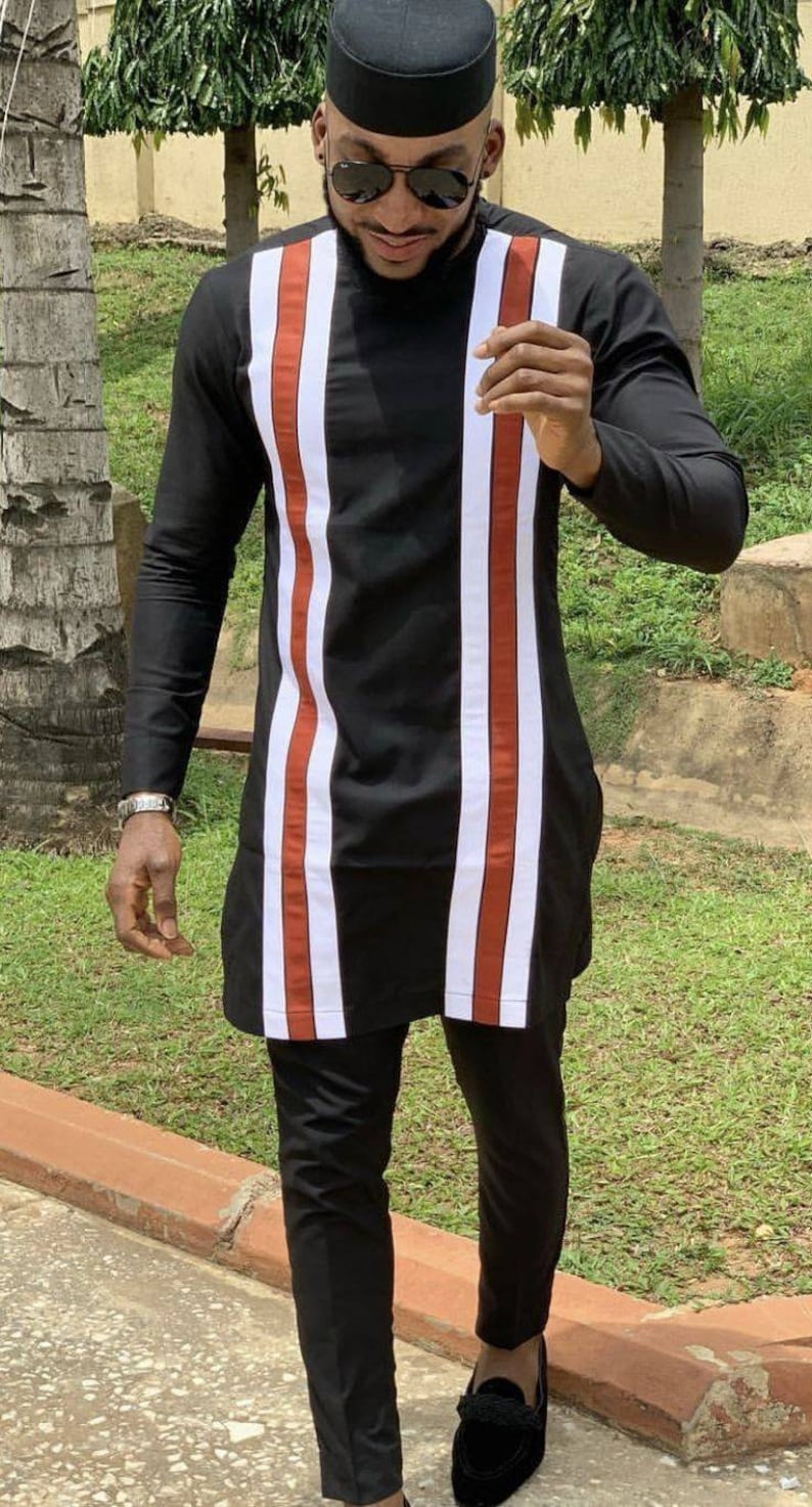 May include: A man wearing a black long-sleeved shirt with white and red vertical stripes, black pants, and black loafers. He is also wearing a black hat and sunglasses.