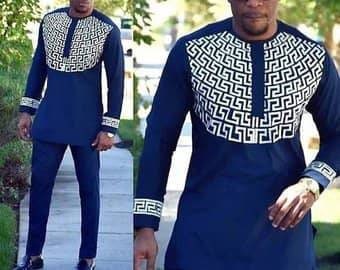 Può includere: Tunica blu navy a maniche lunghe e pantaloni abbinati. La tunica presenta un motivo geometrico bianco sul petto e sui polsini. L'outfit è in stile tradizionale, adatto alle occasioni formali.