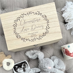 May include: A wooden keepsake box with a floral wreath design engraved on the lid. The box is personalised with the name "Clementine Luna Davies", the date "25th April 2022", and the time "9:04pm". The box also includes the baby's weight, "7lbs 11oz".