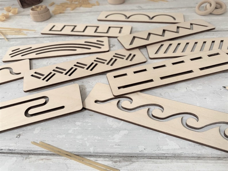 May include: A set of nine wooden stencils featuring various patterns, such as wavy lines, zigzags, and straight lines. The stencils are crafted from light brown wood and are displayed on a white surface.