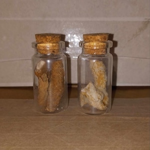 May include: Two small glass bottles with cork stoppers, each containing a piece of dried orange peel.