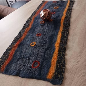 Könnte beinhalten: Ein dunkelblauer Tischläufer mit orangefarbenen und gelben Streifen und einem schwarzen Leopardenmuster. Der Läufer hat mehrere orangefarbene und rote Filzkreise, die darauf genäht sind. Ein kupferfarbener Kerzenhalter liegt auf dem Läufer.