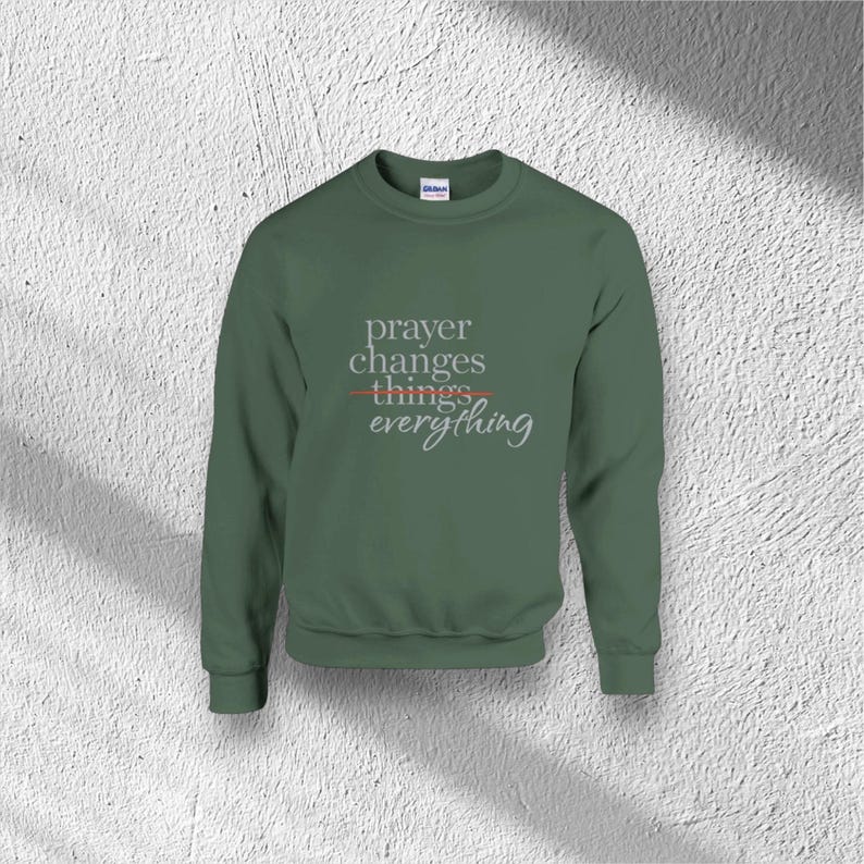 Puede incluir: Una sudadera verde con el texto "prayer changes things everything" en una fuente estilizada. La palabra "things" est&aacute; tachada con una l&iacute;nea roja. La sudadera es de color liso y tiene cuello redondo.