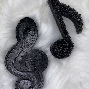 May include: Two black treble clef music note ornaments. One is smooth and the other is textured.