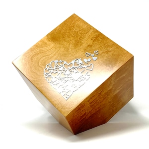 Peut inclure: Une boîte en bois avec un motif en forme de cœur composé de petits cœurs. La boîte est de couleur brun clair et a une finition lisse.