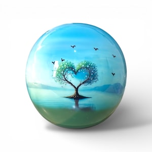 May include: A clear glass sphere with a painted landscape scene. The scene features a tree with a heart-shaped canopy, set against a blue sky and water. Small black birds are scattered across the sky. The sphere has a glossy finish.