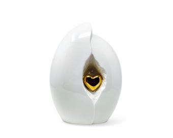 May include: A white ceramic sculpture with a gold heart-shaped detail. The sculpture has a smooth, glossy finish and a split design revealing the golden heart. The overall shape is rounded and organic.