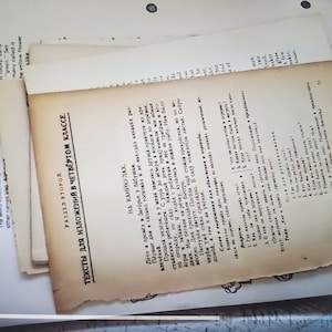 以下が含まれることがあります： ロシア語で書かれた古い黄ばんだ紙の束。一番上の紙には「4年生作文のためのテキスト」というタイトルと「小さな川で」という副題が書かれている。