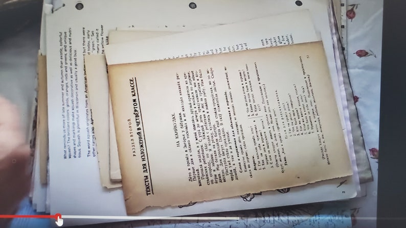 以下が含まれることがあります： ロシア語で書かれた古い黄ばんだ紙の束。一番上の紙には「4年生作文のためのテキスト」というタイトルと「小さな川で」という副題が書かれている。