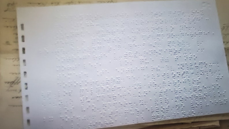 以下が含まれることがあります： 表面全体に点字と呼ばれるパターンで盛り上がった点が付けられた白い紙。紙の左端に一列の穴が開いている。