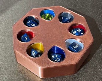 Puede incluir: Una bandeja de dados octogonal de color cobre con ocho compartimentos, cada uno con un dado de color diferente. Los dados son azules, verdes, amarillos y rojos.