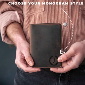 May include: A brown leather journal with a monogrammed initial "J" in a wreath design. The journal is held in a person's hands.